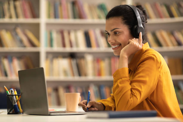 istock Positive mixed race lady sitting in library, using laptop and taking notes, watching lecture or webinar 1471477946