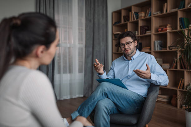 ernsthafter junger kaukasischer mann arzt psychologe berät frau in modernen klinik interieur, freiraum - psychiatrie und psychotherapie stock-fotos und bilder