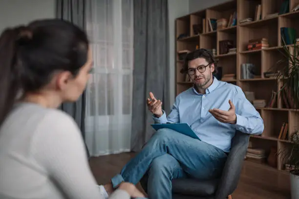 Serious young caucasian guy doctor psychologist advises woman in modern clinic interior, free space. Mental health care, psychological problems, therapy and treatment, professional medical support