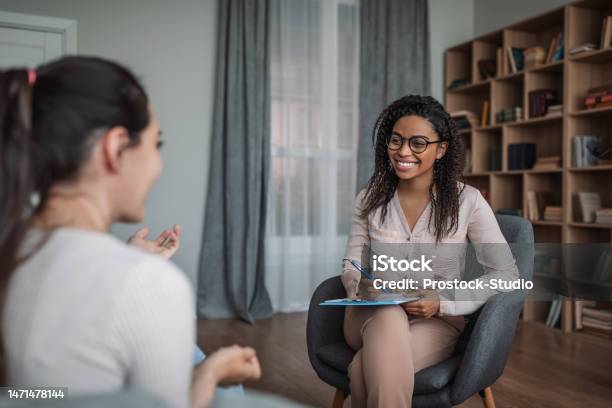 Smiling Young Black Female Doctor Psychologist Consulting European Woman In Modern Clinic Interior Stock Photo - Download Image Now