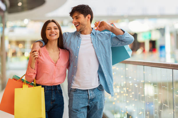 Happy Couple Hugging Doing Shopping Walking Together In Hypermarket Happy Couple Hugging Doing Shopping Walking And Carrying Shopper Bags Enjoying Weekend Together In Modern Hypermarket. Shopaholics Spouses Buying Clothes In Mall. Consumerism shopping stock pictures, royalty-free photos & images
