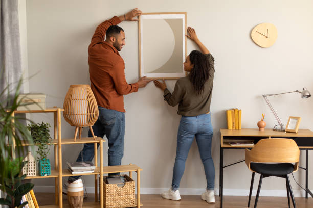 cónyuges millennials negros cuelgan un póster en la pared juntos en casa - decorar fotografías e imágenes de stock