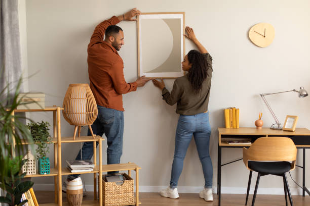 чернокожие супруги-миллениалы висят плакат на стене вместе дома - home decorating фотографии стоковые фото и изображения