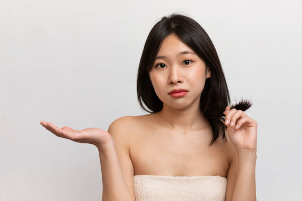Hair care concept. Upset young korean lady checking her hair, having problem of thinning hair, hair loss stock photo