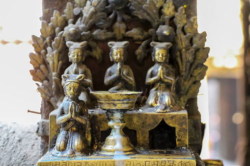 Close-up view of bronze candlestick with small praying people figurines in Hiranya Varna Mahavihar (The Golden Temple) temple. Soft focus. Religious heritage theme.