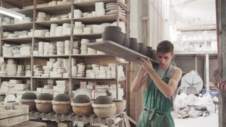 Man walking with a tray of clay bowls in a ceramics factory