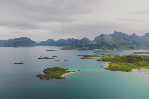 Dramatic view of the beautiful remote beach with turquoise ocean and view of the green mountains peaks in Nordland, Northern Norway