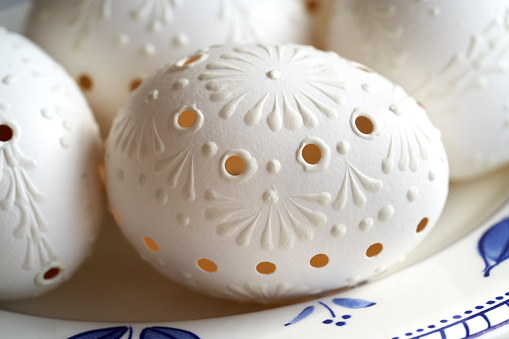 Closeup of white Easter egg decorated with wax with drilled holes on a plate