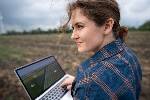 Farmer with laptop on the field. Wind turbines on a horizon. Smart sustainable farming and agriculture digitalization