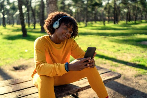 A girl in a yellow tracksuit listening to music in the park with headphones. stock photo
