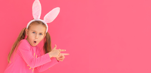 Easter shopping. Excited emotion surprise adorable child girl in bunny ears rabbit costume point hand finger up to isolated pink background. Kid Sale discounts. children attentive