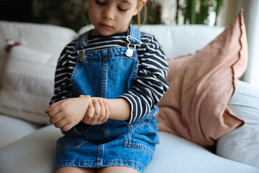 Midsection of an unrecognizable caucasian girl wearing a purple t-shirt is touching her wrist in pain on the sofa