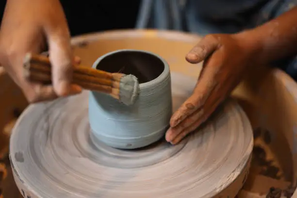 Close up on skillful hands making and sculpting pottery jar on potter wheel with tools and water in workshop, Creative and artwork, Handmade craft
