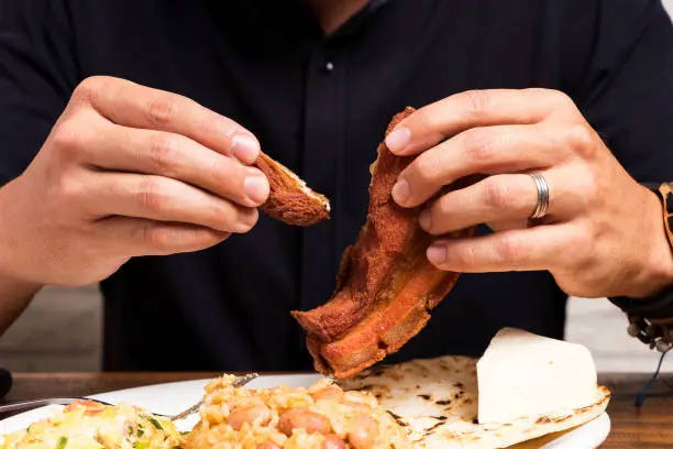 Photo of Hands of man eating fried pork at lunch in Colombia