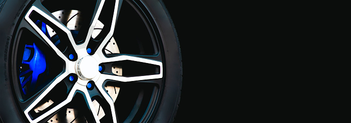 Closeup of the wheel of a sports car on a black background, panoramic banner with copy space