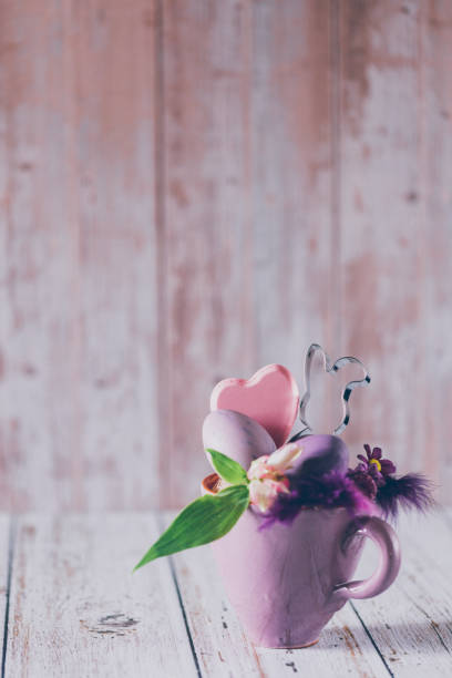 istock Rustic purple cup with an Easter bunny cookie cutter, daisies, feathers a heart shape and purple Easter eggs on wooden background with copy space 1471490084