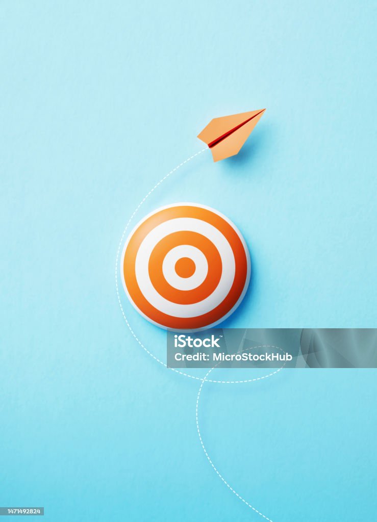 Paper Plane Flying Around An Orange Bull's Eye Target On Blue Background Paper plane flying around an orange bull's eye target on blue background, Social media and networking concept. Aspirations Stock Photo