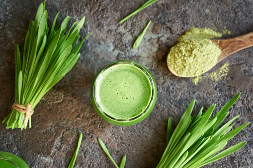 A glass of fresh green barley grass juice with blades and powder, top view
