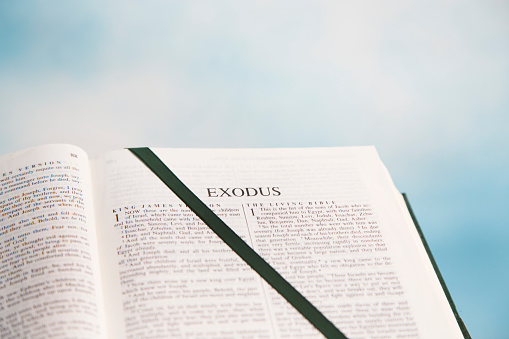 Open Bible to the book of Exodus in the Old Testament.  Blue sky with white clouds in background.  Dark Green Satin Ribbon marks the page.