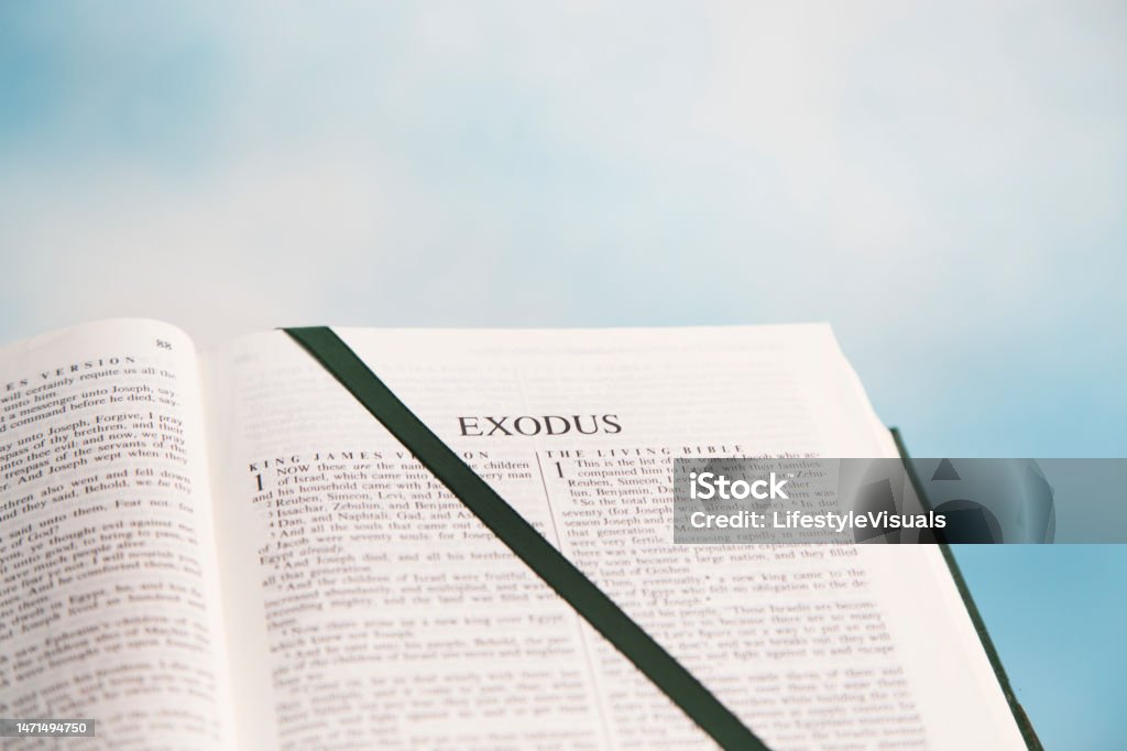 Open Bible to the book of Exodus in the Old Testament.  Blue sky with white clouds in background.  Dark Green Satin Ribbon marks the page. Bible Stock Photo