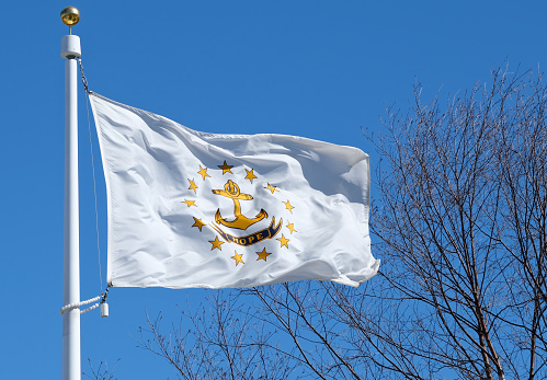 State flag of Rhode Island against a blue sky background with tree branches