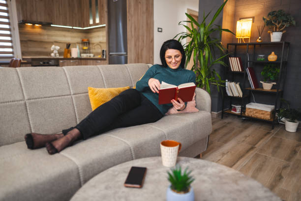 istock White woman reading a book while sitting on a living room sofa 1471501728
