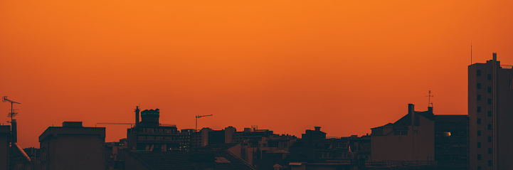 Panoramic view of a bright orange sunset, contrasting silhouettes of the city's edifice; a sandstorm appearing as if in the desert, the dust and sand envelop the city in an almost otherworldly haze