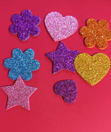Colorful glitter foam stickers in the shape of heart, stars and flowers on red background