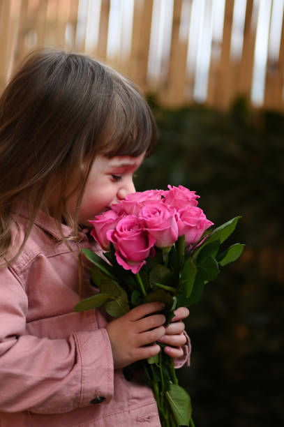 vue latérale d’une jolie petite fille qui sent les roses. - aromatherapy single flower flower holding photos et images de collection