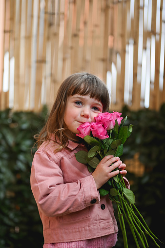 little girl embracing a bouquet with pink roses outdoors.