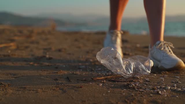 Woman volunteer collects garbage on the beach. Environmental pollution.