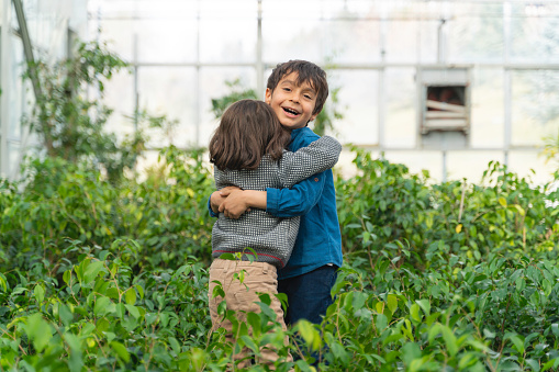 image of happy two brothers hugging among potted plants grown in greenhouse. cute boy with long messy hair. two brothers spend happy time together. Shot in natural light with a full-frame camera.