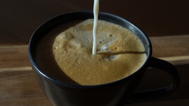 Close up of pouring almond milk in a cup with coffee