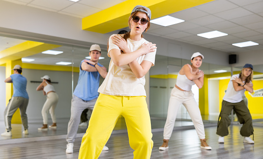 Class of young fit teenagers in casual wear dancing together during training in spacious studio