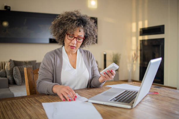 istock Mature woman using calculator while going through bills and home finances 1471519748