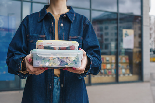 Woman holding reusable plastic containers with salad and snacks outdoors