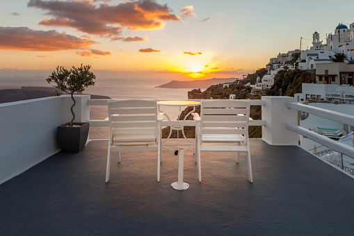 Two chairs face the sun as it sets over the Aegean Sea in Santorini Greece