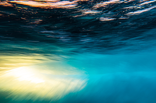 An abstract artistic scene of a wave breaking underwater in dramatic golden light. Photographed with slow shutter in camera technique.