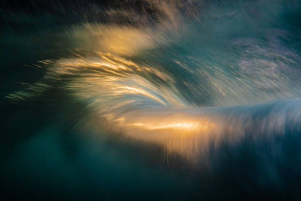 An abstract artistic scene of a wave breaking underwater in dramatic golden light stock photo