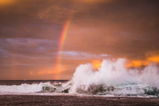 istock Ocean waves colliding under a dramatic storm pink and gold sky at sunset with rainbow 1471531216