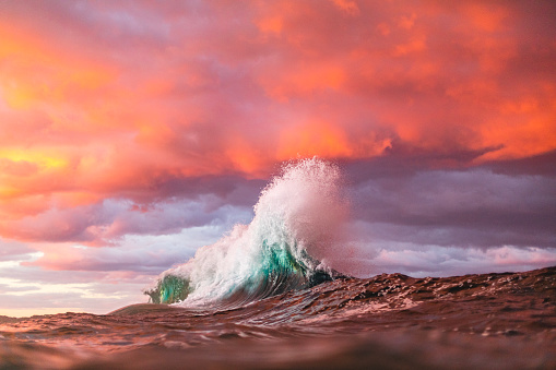 Ocean waves colliding creating unique water pattern under a dramatic pink and gold sky at sunset. Beauty in nature scene. Shot on the south east coast of Australia.