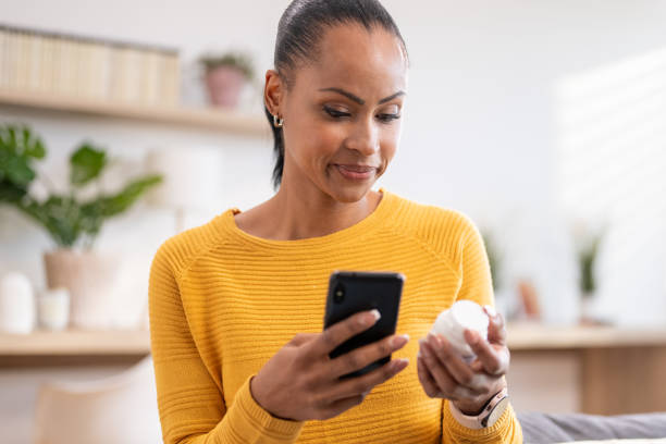 Woman searching pills instruction on smartphone Woman holding pills bottle and searching medications dosage instruction online on smartphone in living room pill prescription capsule prescription medicine stock pictures, royalty-free photos & images