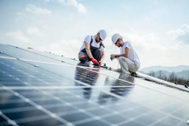 Team of two workers on a house's roof installing solar panels.