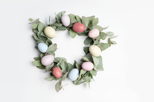 A beautiful traditional Easter wreath made of eucalyptus leaves and pastel easter eggs, on a white background, photographed flat lay.