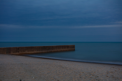 Concrete jetty at an angle leading to massive body of water with sandy beach in Chicago