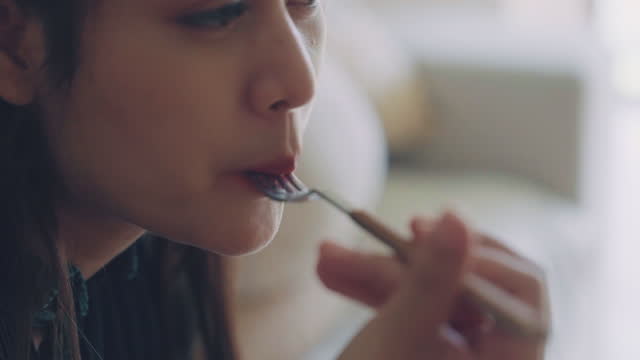 Close-up of Young happy asian woman eating healthy salad sitting on the sofa in living room.
