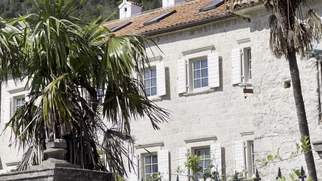 Old stone building with wooden shutters and palm trees in the garden