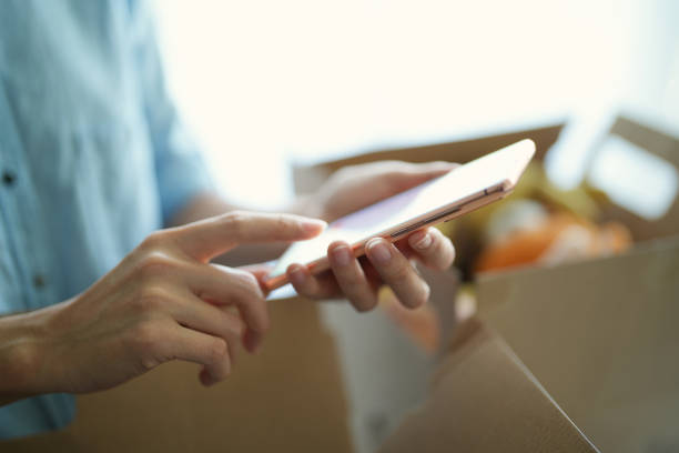 istock Asian female woman using smartphone while packing or unpacking as she is moving into a new place house. she is using her smartphone chatting with friends and family or finding a delivery service nearby. 1471555537