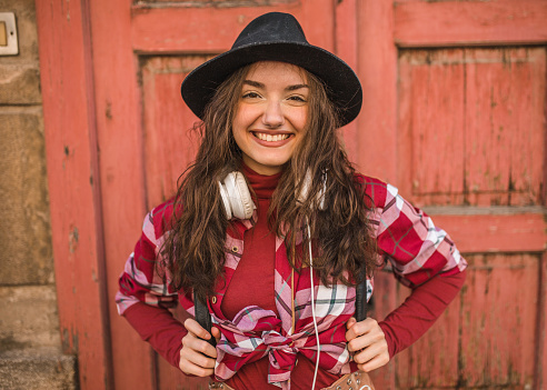 Young smiling female tourist dressed in a plaid shirt enjoying listening to music