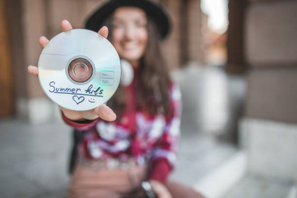 zbliżenie płyty kompaktowej z letnimi przebojami muzycznymi, trzymane przez młodą, uśmiechniętą kobietę - cd audio zdjęcia i obrazy z banku zdjęć